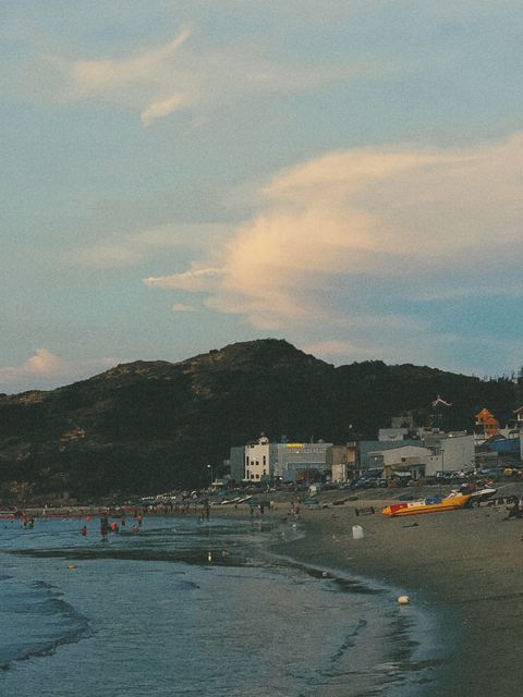 Quiet beach at dusk, a dark hill and seaside buildings under a pink-lit cloud — shot on ELEV RAIL