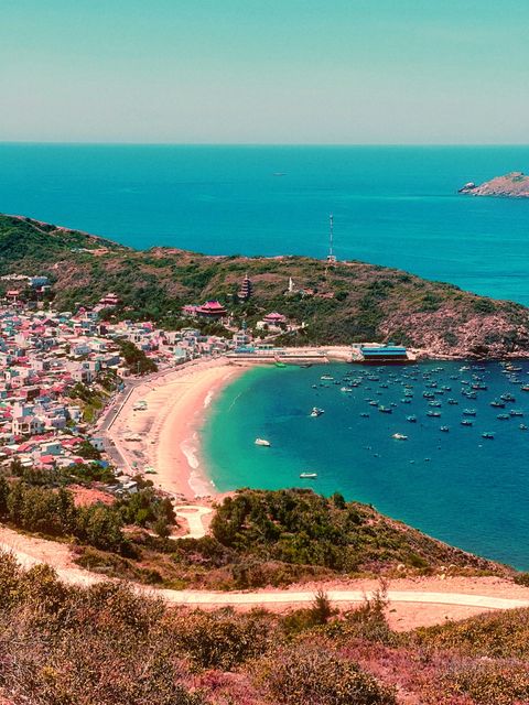 Hilltop view over a fishing village and crescent beach, a dirt road winding through the scrub — shot on B 01