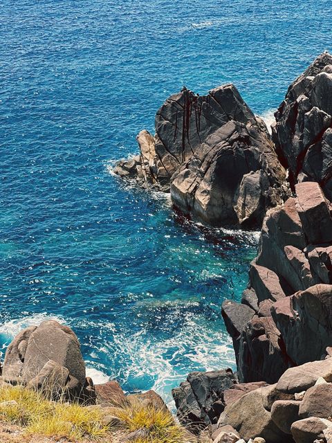 Dark rocks rising from deep blue water, white foam around their base — shot on A AFX