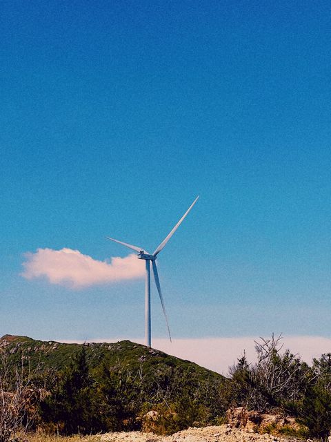 A single wind turbine on a green hill beside a small white cloud — shot on ELEV DUSK