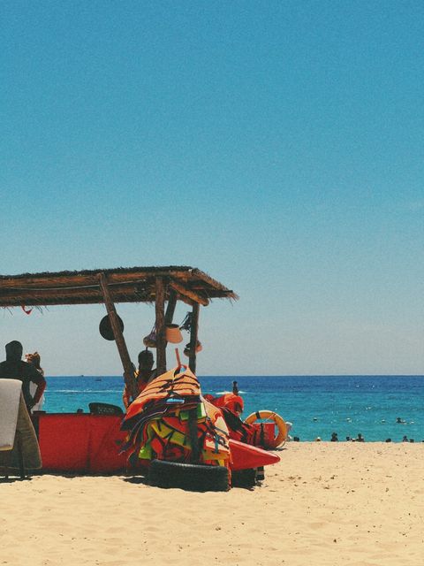 Thatched beach hut stacked with life jackets beside a red boat on bright sand — shot on ELEV RAIL